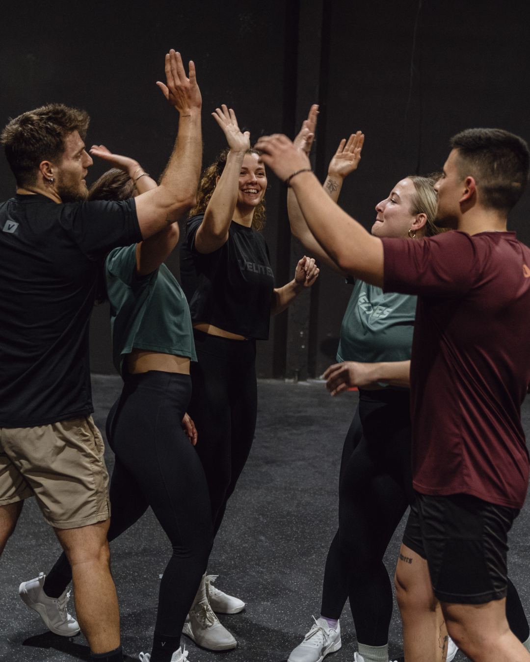 Group of people in athletic wear giving each other high fives on a dark background