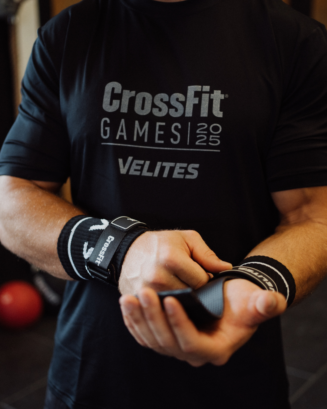 Person wearing a CrossFit shirt and wrist wraps, holding Crossfit handripgs.